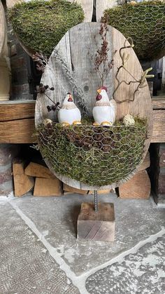 three white birds sitting in a wire basket on top of a wooden stand with moss