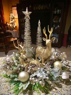 a christmas centerpiece with gold deer, pine cones and silver baubles on a table