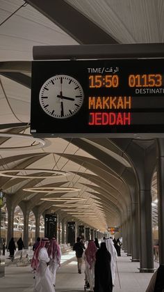 there is a large clock in the middle of an airport terminal with people walking by