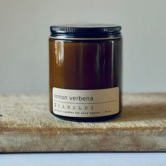 a candle sitting on top of a wooden table next to a white wall with a label that reads lemon verbbena candles