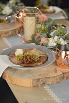 a table topped with plates filled with grapes and cheese on top of a wooden slab