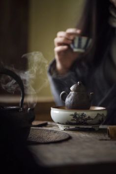 a woman sitting at a table with a tea pot and cup