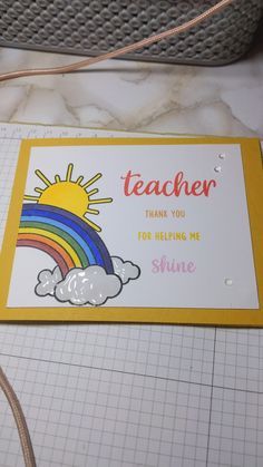 a teacher thank you card with a rainbow and clouds in the background on a cutting board