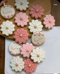 decorated cookies are arranged on top of a white plate and wooden table with pink and white flowers