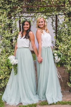 two women standing next to each other in front of a trellis covered arbor with flowers