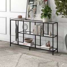 a black metal shelf with books and vases on it in front of a white wall