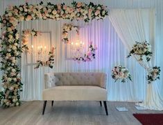 a white couch sitting in front of a wall covered in flowers and greenery next to a chandelier