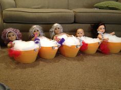 five dolls are sitting in buckets filled with foamy bubbles on the floor next to a couch