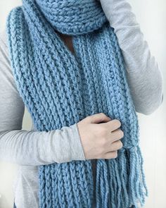 a woman wearing a blue knitted scarf and holding her hand on her shoulder,