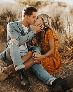 a man and woman are sitting on the ground in front of some dry grass with their noses to each other