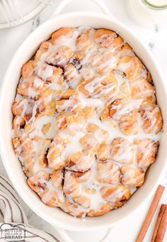 cinnamon rolls with icing in a white casserole dish next to cinnamon sticks