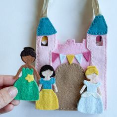 a hand holding a small felt doll with a castle in the background and princesses on it