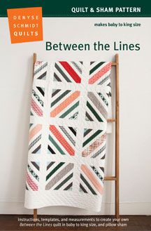 a white quilt hanging on a wall next to a wooden ladder with an orange and green striped design