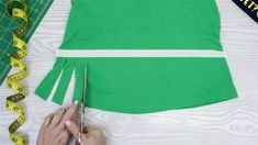 a person cutting up a green dress with scissors and tape on the table next to it