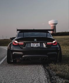 the back end of a black bmw car parked in front of a large water tower