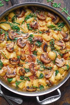 a pan filled with potatoes and mushrooms on top of a wooden table