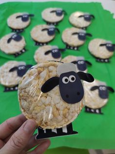 a hand holding up a cookie shaped like a sheep with cookies in front of it