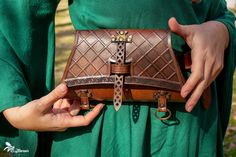 a woman in green dress holding a brown leather purse with chains on the front and sides