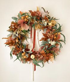 a wreath is hanging on the wall with leaves and berries around it, as if in autumn or fall