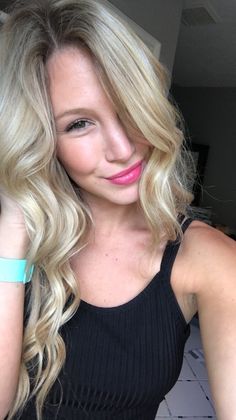 a woman with long blonde hair wearing a black tank top and blue bracelets is looking at the camera