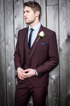 a man in a suit and tie standing next to a wooden wall wearing a boutonniere