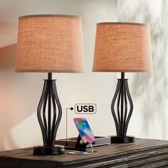 two lamps on top of a wooden table with an iphone charging in the charger