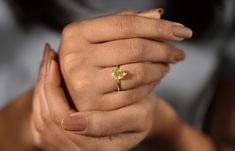 a woman's hand holding an engagement ring with a yellow diamond on it,