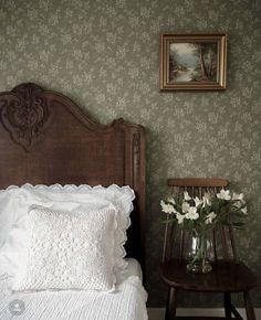 a bed with a wooden headboard next to a small table with flowers on it