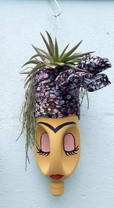 a yellow mask hanging from the side of a wall with an air plant on it's head