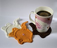 two crocheted coasters next to a cup of coffee on a white surface