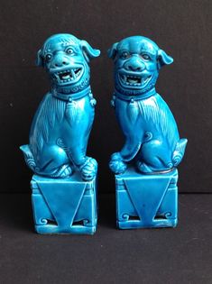 two blue dog figurines sitting on top of each other in front of a black background