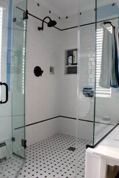 a white tiled bathroom with black and white tile flooring, glass shower door, and sink