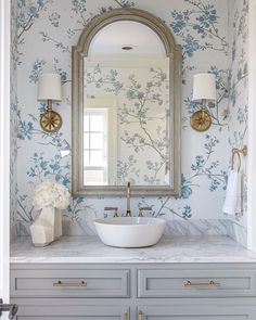 a bathroom with blue and white wallpaper, gold faucet, marble counter top