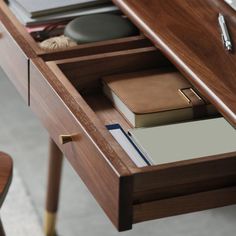 a wooden desk with books, notebooks and pen on it's drawer next to a chair