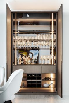 an open cabinet filled with lots of wine glasses and champagne flutes in front of a white chair