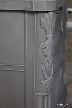 a close up view of an ornate design on a gray painted cabinet with wood flooring