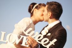 a bride and groom kissing with the word love spelled out in front of them on their wedding day