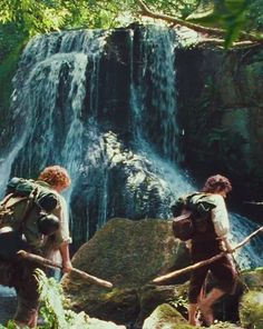 two people with backpacks standing in front of a waterfall