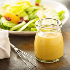 a glass jar filled with dressing next to a bowl of salad