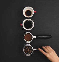 three cups of coffee and two spoons on a black surface with one being stirred by the other