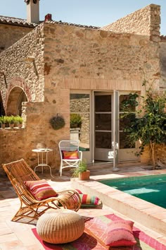 an outdoor pool area with chairs and pillows on the ground next to it, surrounded by stone buildings