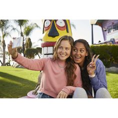 two young women taking a selfie in front of a totem pole with their fingers up