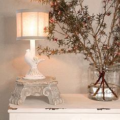 a white dresser topped with two vases filled with flowers and a lamp next to it