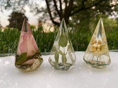 three glass vases with flowers in them sitting on a white table outside near some grass