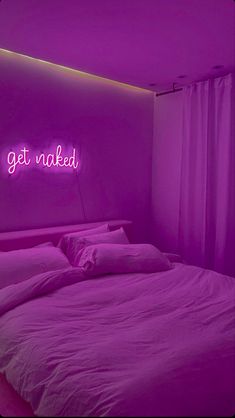 a bed in a room with a neon sign on the wall above it that says get naked