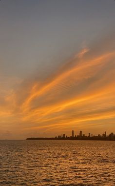 the sun is setting over the city skyline as it reflects in the calm ocean water