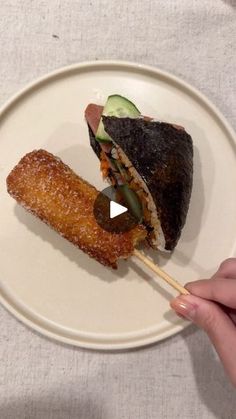 a person holding a piece of food on a white plate with a toothpick in it