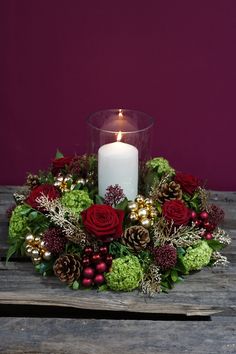 a candle sits in the center of a wreath with red roses, greenery and berries