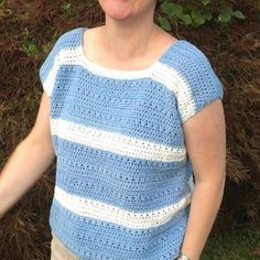 a woman standing in front of a bush smiling at the camera, wearing a blue and white crochet top