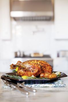 a roasted chicken on a black plate with silverware and utensils in the background